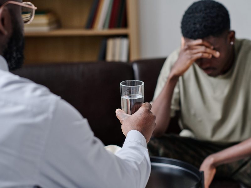 African psychotherapist giving glass of water to support patient at office during psychotherapy session